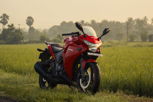 Free Red Honda motorcycle parked in a vibrant green field in Kollengode, Kerala. Stock Photo