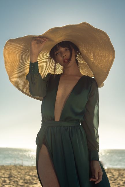 Elegant woman in green dress and sun hat posing on a sunny beach.