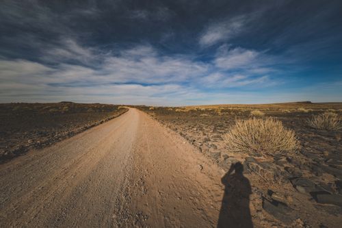 Free Expansive desert landscape with a solitary dirt road under a vibrant sky. Captured with a shadow silhouette. Stock Photo