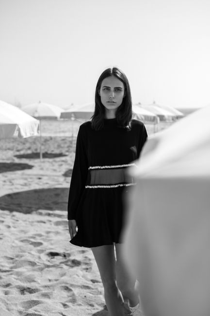 Stylish woman in black dress posing on a sunny beach day.