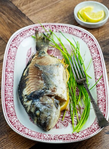 Whole baked fish with chives and lemon on a patterned platter — photo by Elsa silva on Pexels