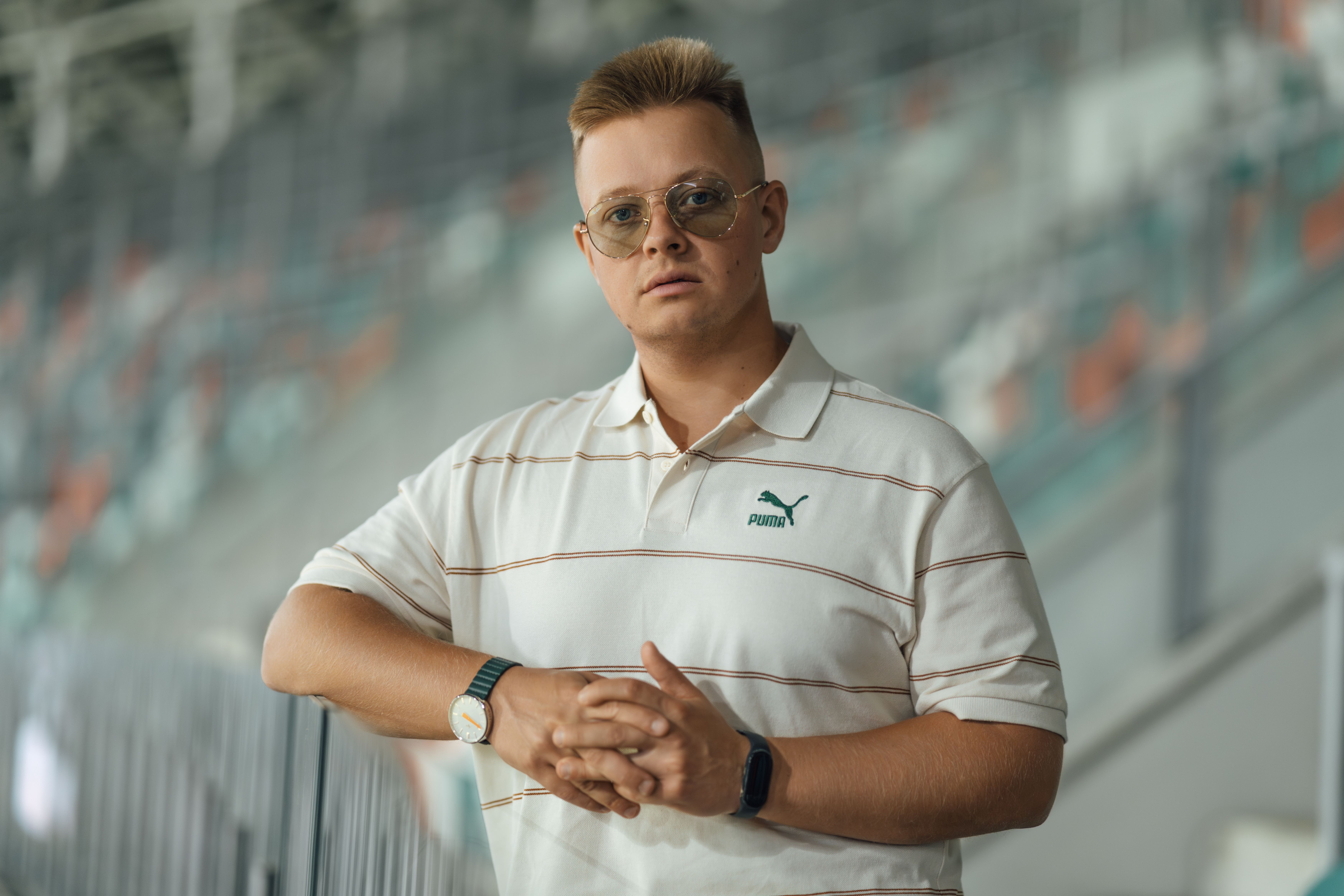 Man in white sports polo and glasses posing confidently indoors.