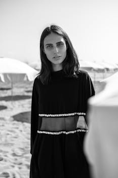 一位时尚女士在阳光明媚的海滩上摆出优雅的黑白造型，展现时尚与美丽