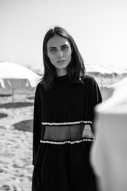Stylish woman poses elegantly on a sunny beach in black and white, showcasing fashion and beauty.