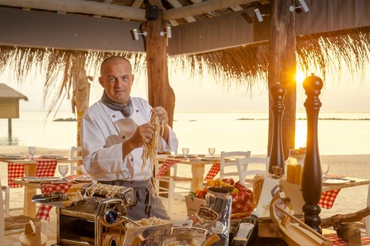 Chef making fresh pasta beside a beach sunset, capturing culinary art in a tropical setting.
