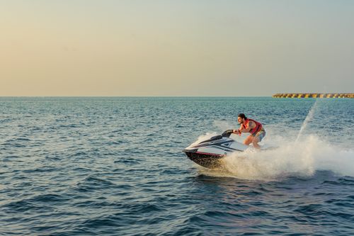 Free Man enjoying a thrilling jet ski ride at sea with distant islands under a clear sky. Stock Photo