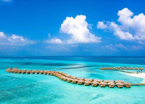A breathtaking aerial shot of tropical overwater bungalows in the Maldives, surrounded by turquoise waters and clear blue skies.