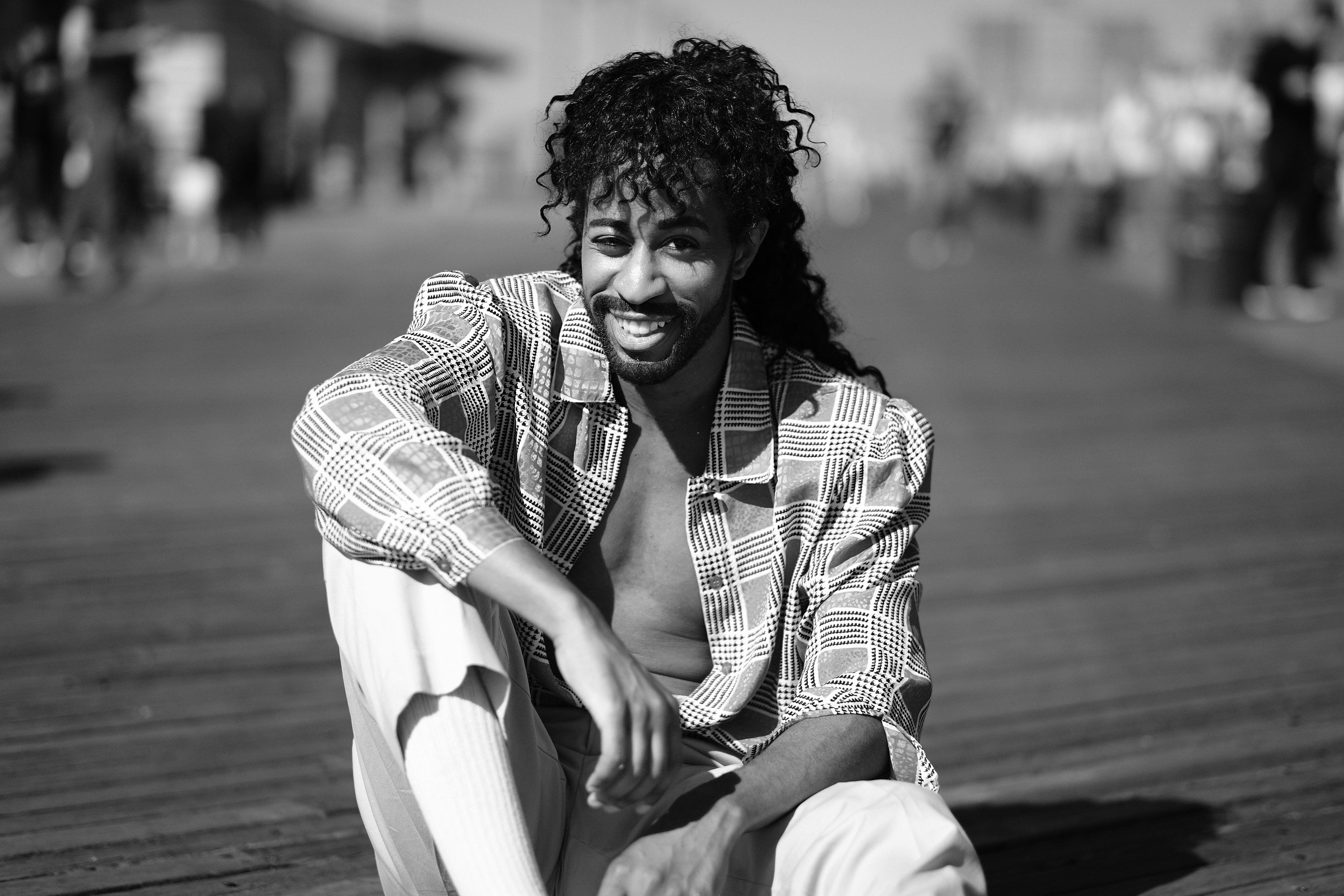 一位卷发的时尚男子面带微笑，在户外摆出单色肖像