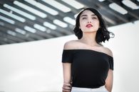 一位身着黑色露肩上衣的优雅女子，在户外时尚的建筑结构前摆出姿势