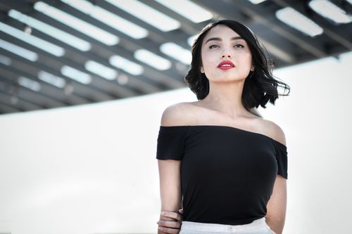 Free Elegant woman in black off-shoulder top posing outdoors under a stylish structure. Stock Photo
