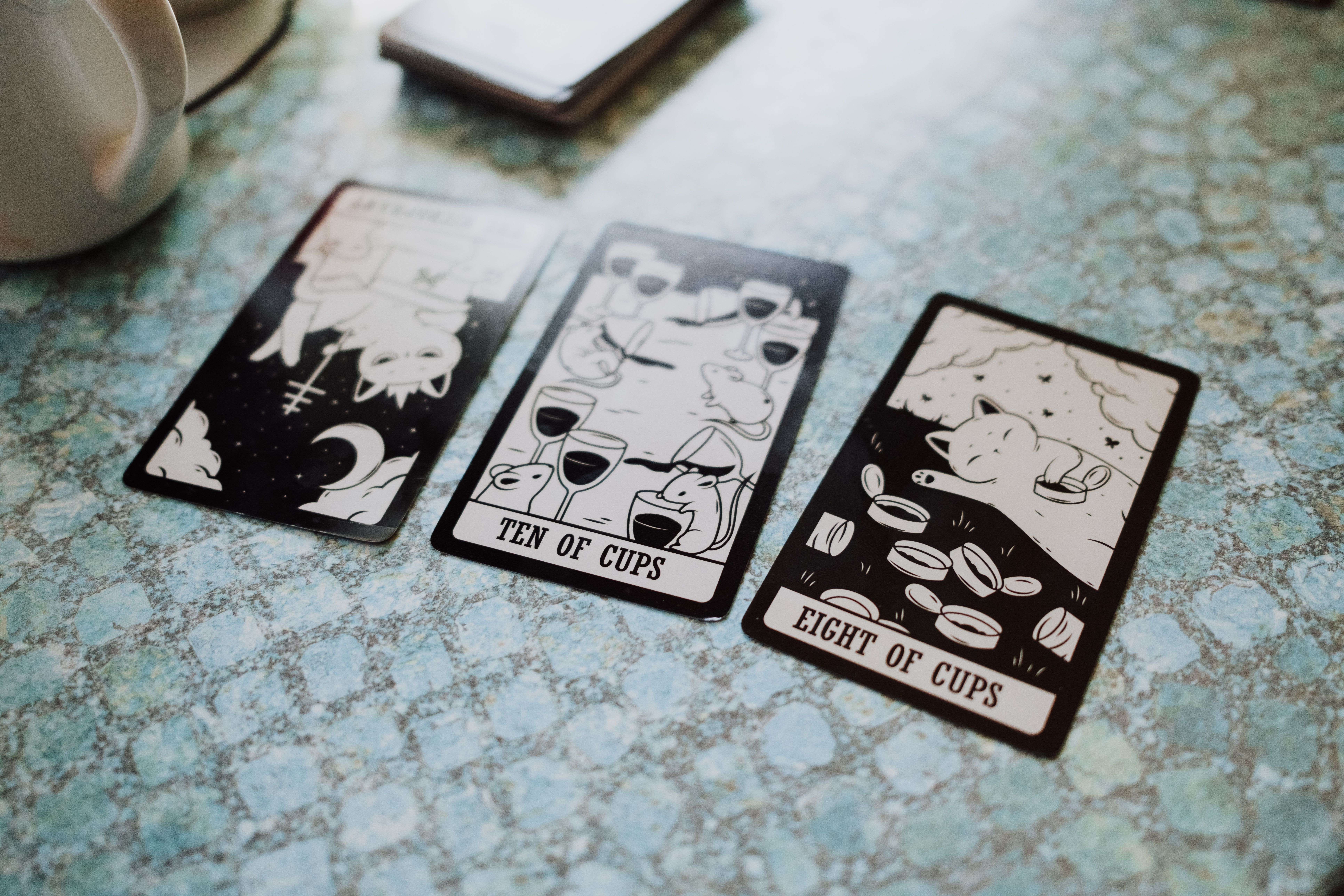 Three tarot cards displayed on a blue textured table surface, featuring cups and illustrations.