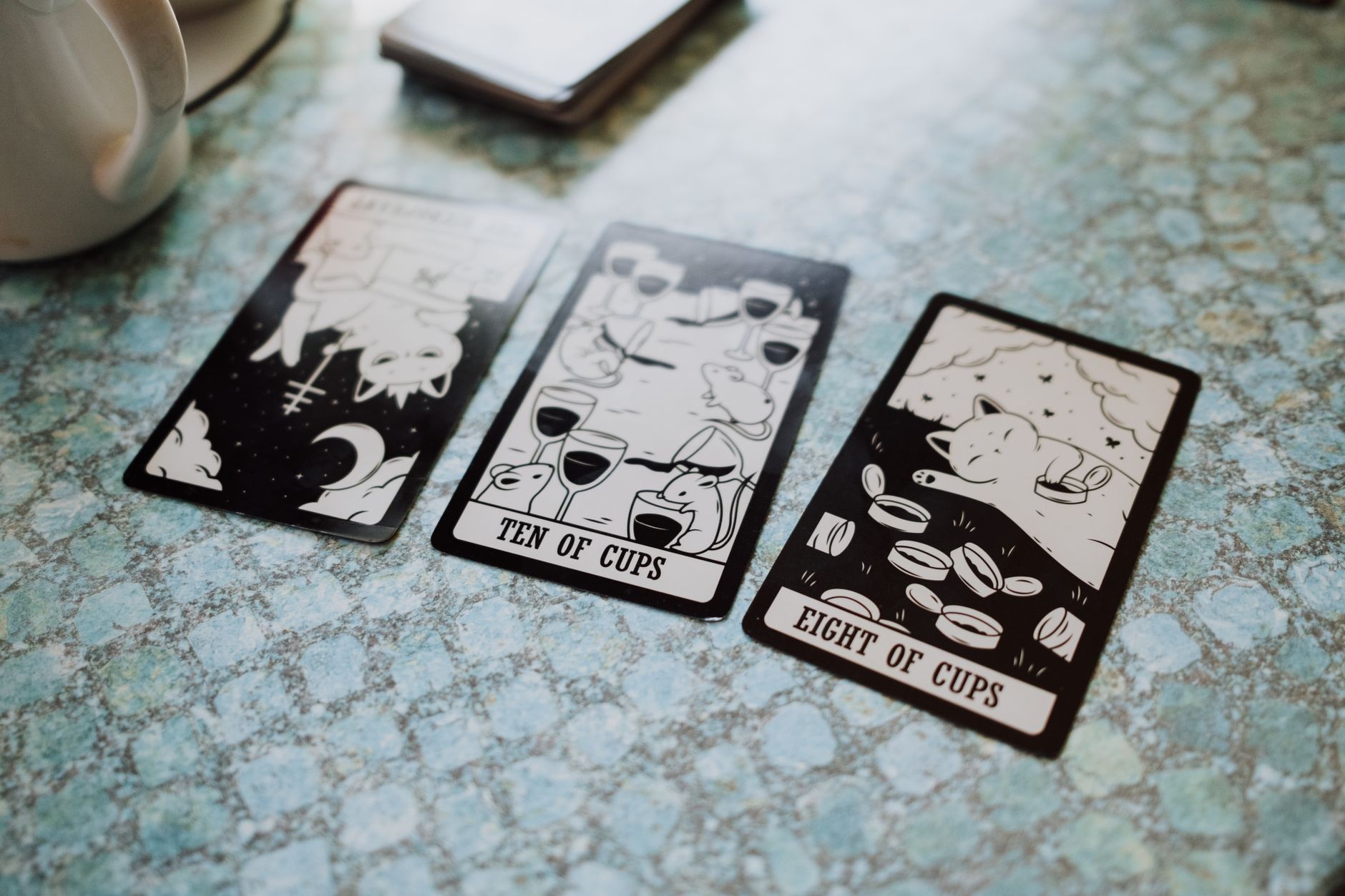 Three tarot cards displayed on a blue textured table surface, featuring cups and illustrations.