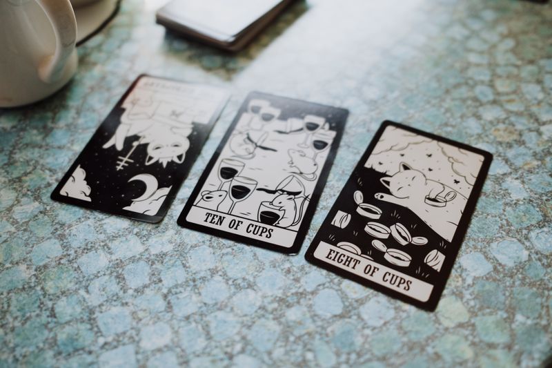 Three tarot cards displayed on a blue textured table surface, featuring cups and illustrations.