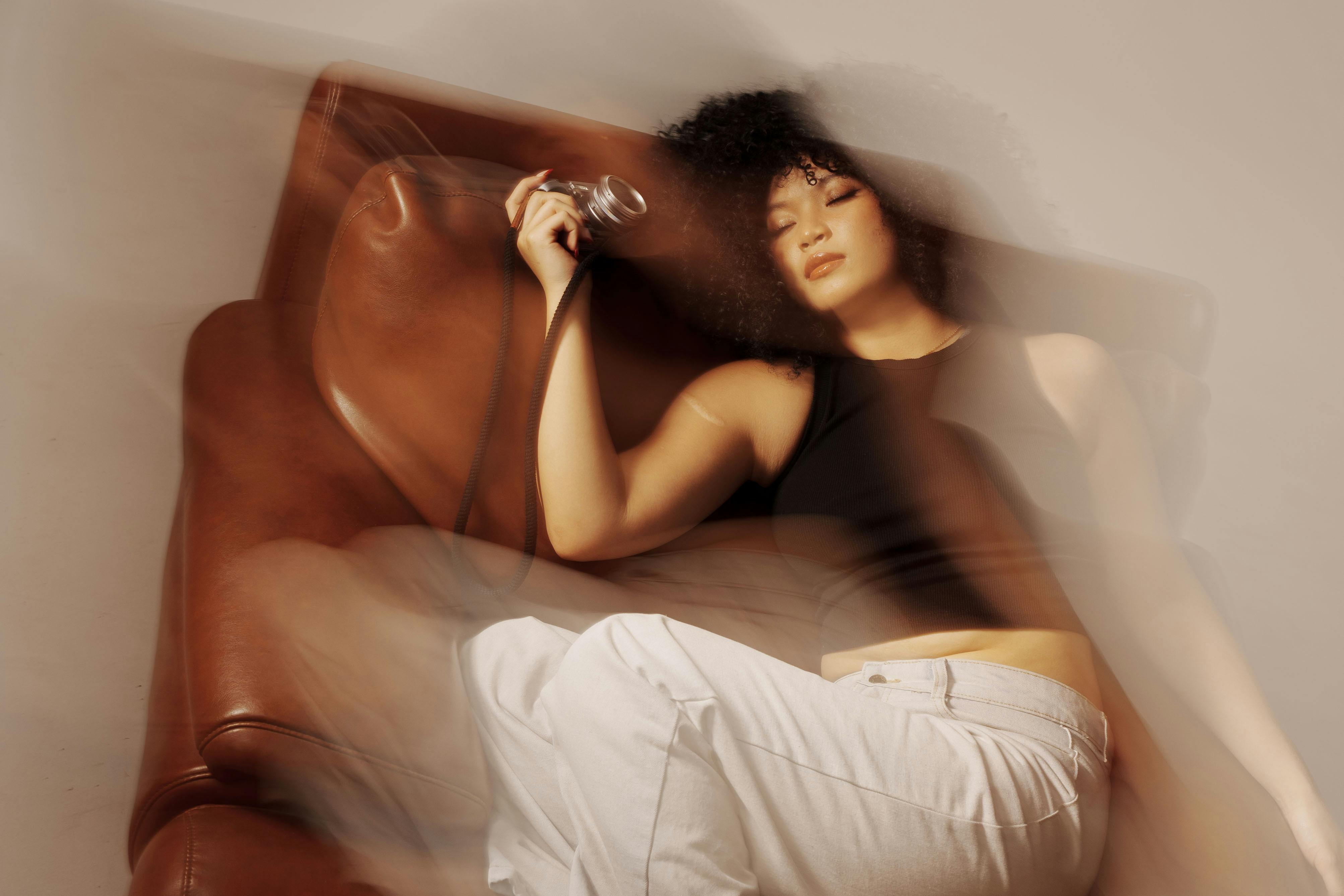 An artistic blurred portrait of a woman relaxing with eyes closed on a leather sofa indoors.