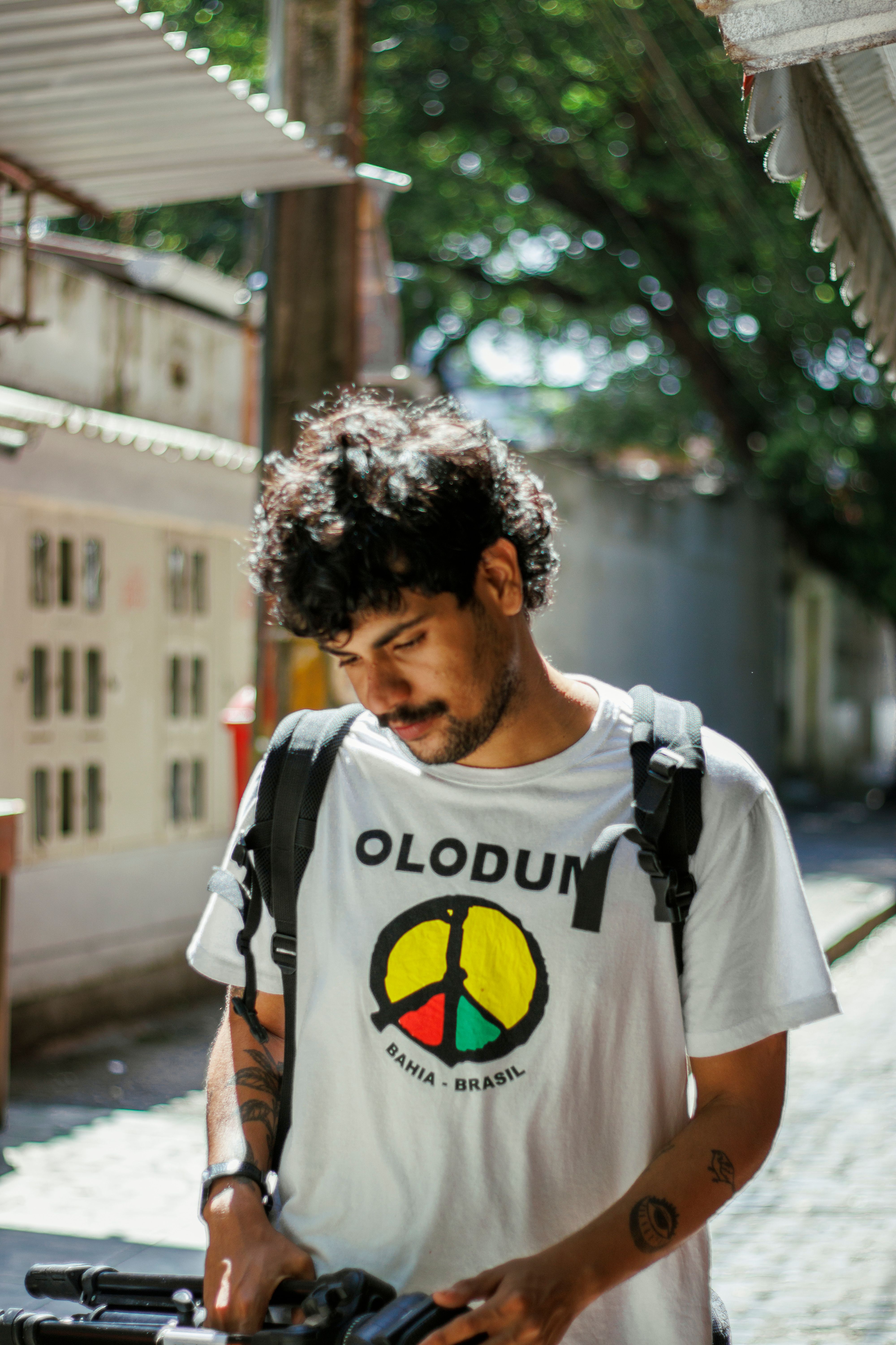 Young man walking in bright urban alley with Olodum shirt and backpack.