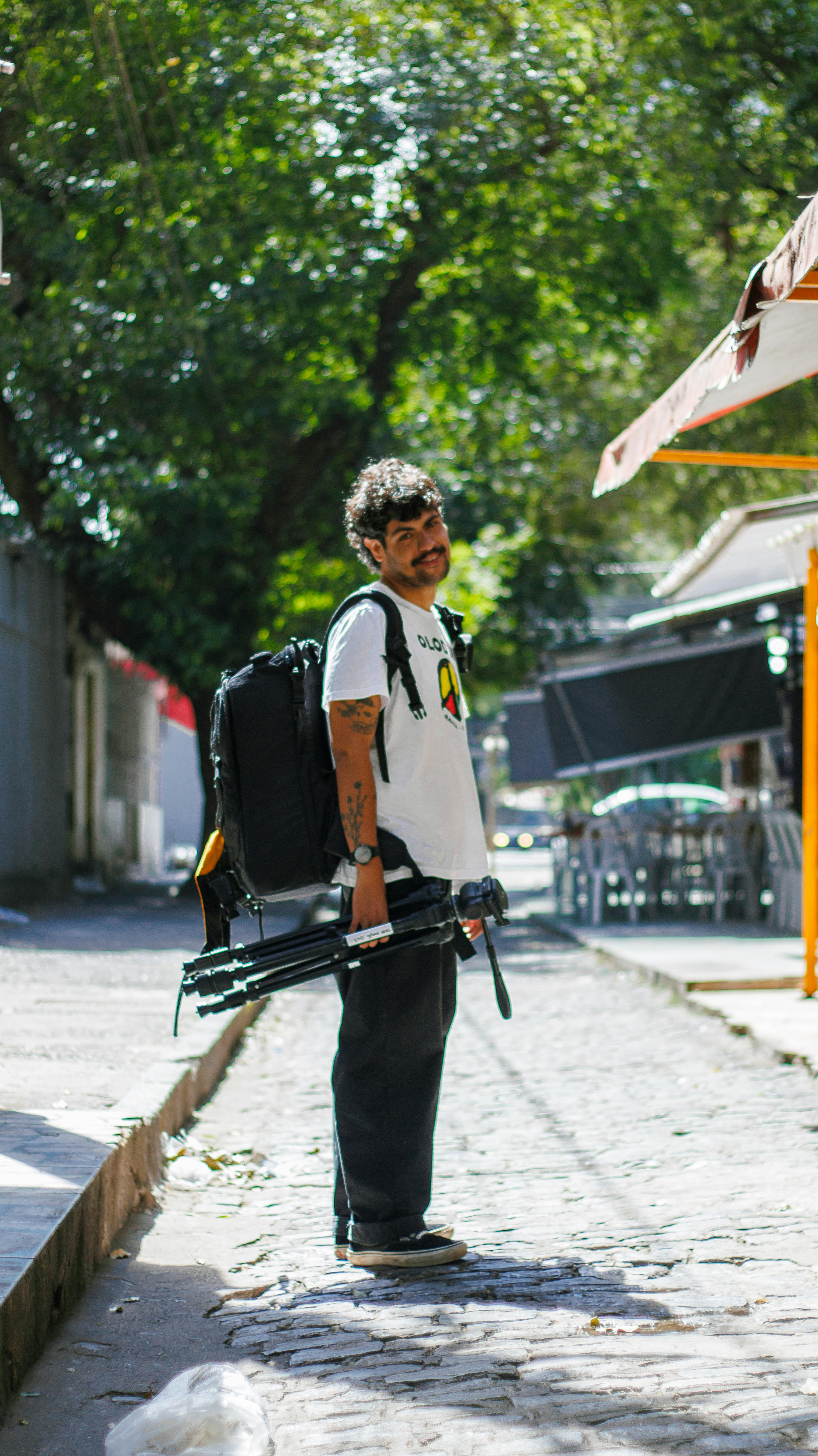 A photographer with equipment stands on a sunlit cobblestone street.