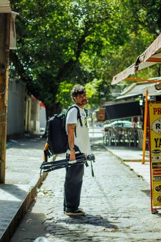 Photographer strolling down a sunlit street with camera gear, capturing urban vibes.