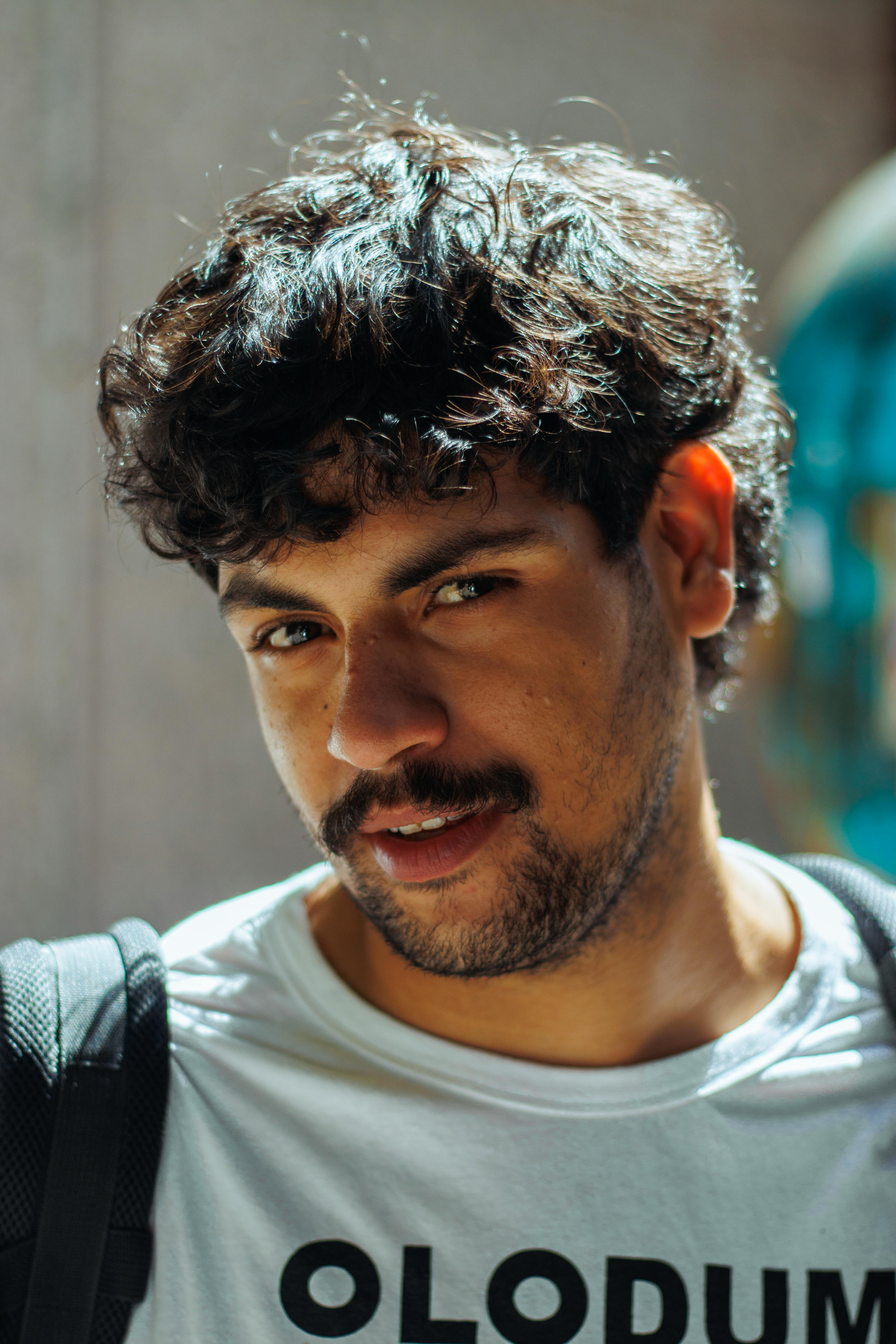Close-up portrait of a man with curly hair wearing an Olodum T-shirt outdoors.