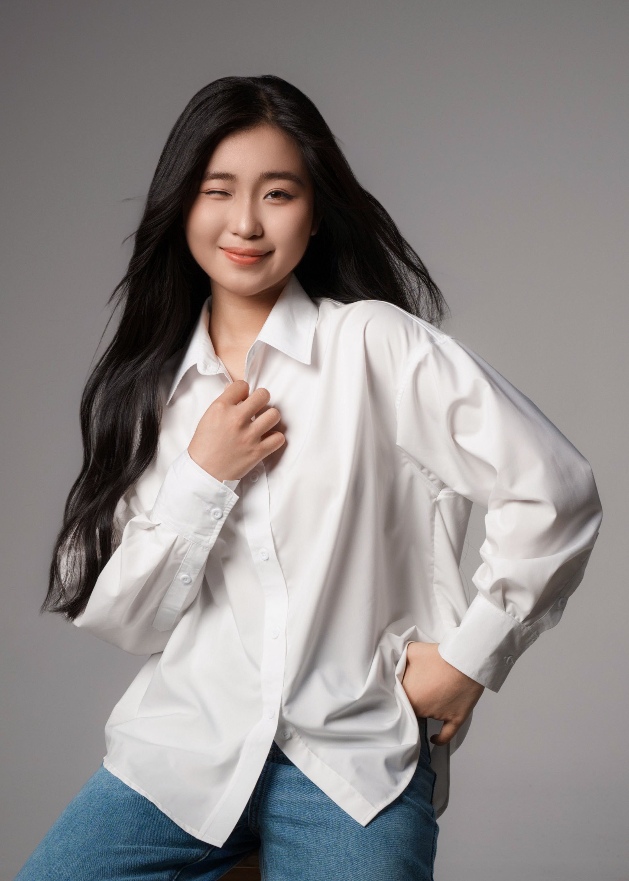 Portrait of a young woman in a white shirt, confidently posing and winking.
