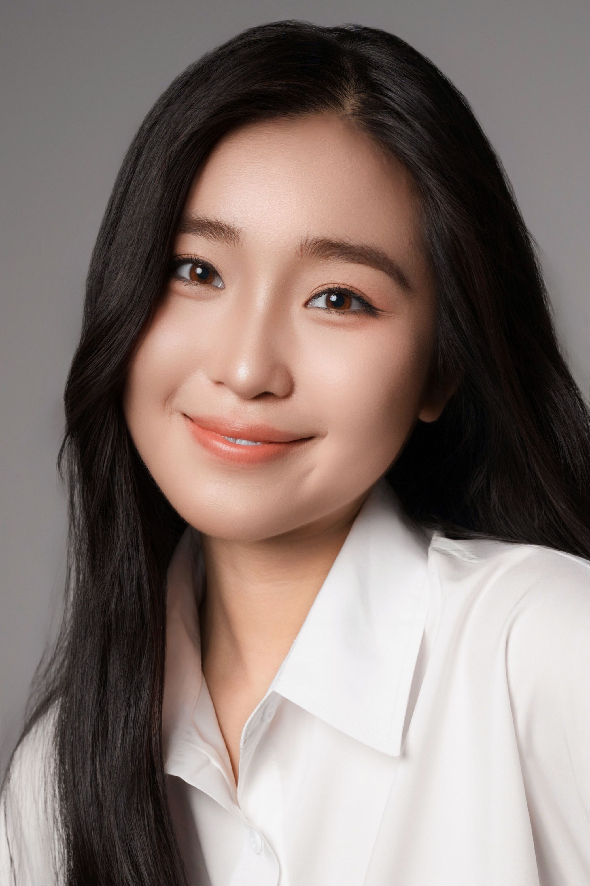 Smiling woman in white shirt with long black hair, neutral background.
