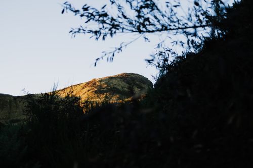 Free A scenic view of a sunlit rocky hill framed by silhouetted foliage, capturing nature's serenity. Stock Photo