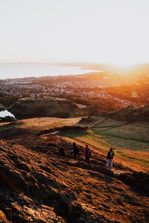 Free A group of hikers ascends Arthur's Seat with Edinburgh's skyline at sunset. Stock Photo