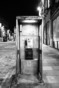 Black and white photo of a graffiti-covered phone booth on an empty Edinburgh street at night.