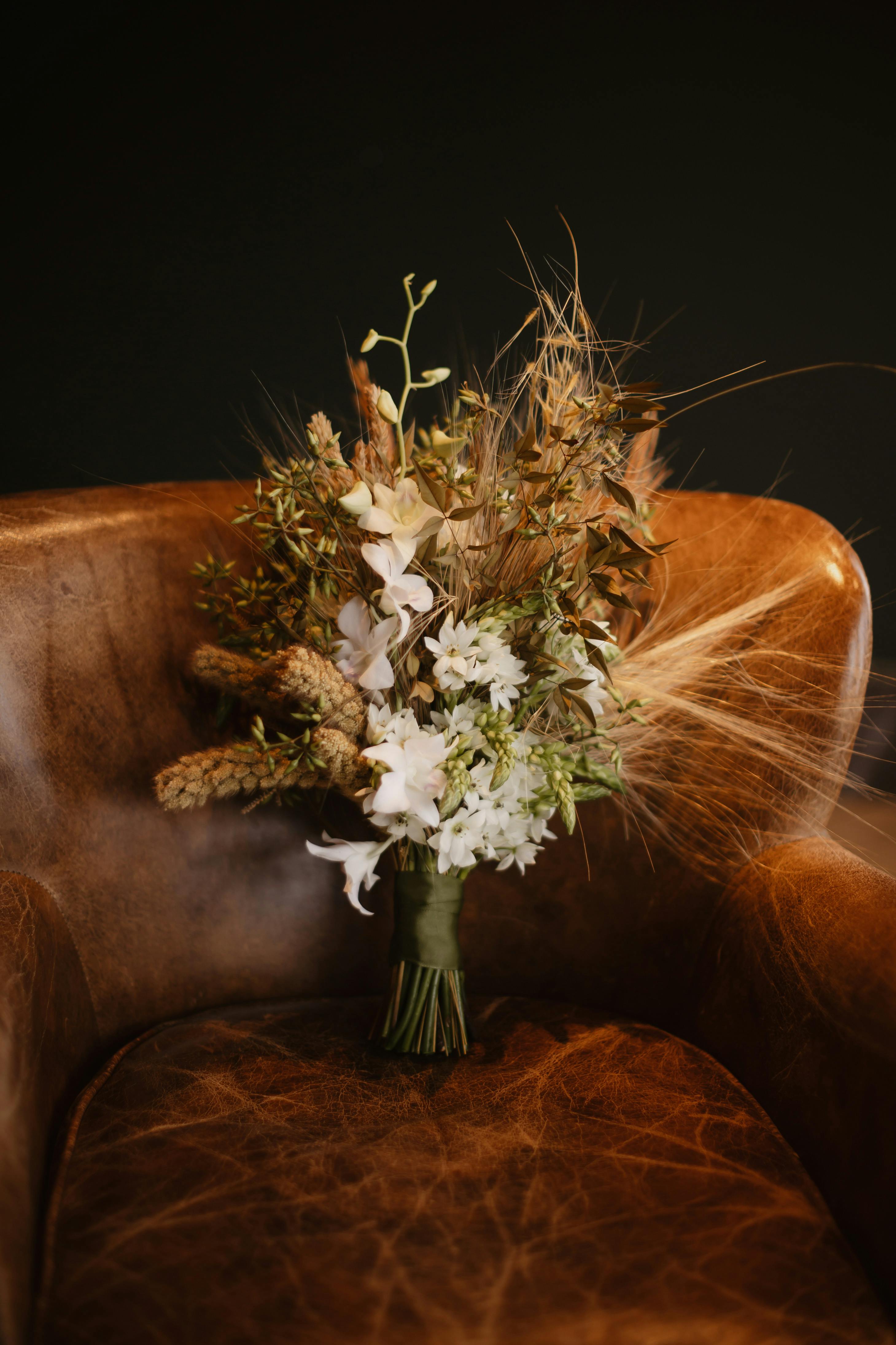 Rustic floral bouquet with mixed textures on vintage leather chair, elegant and artistic.