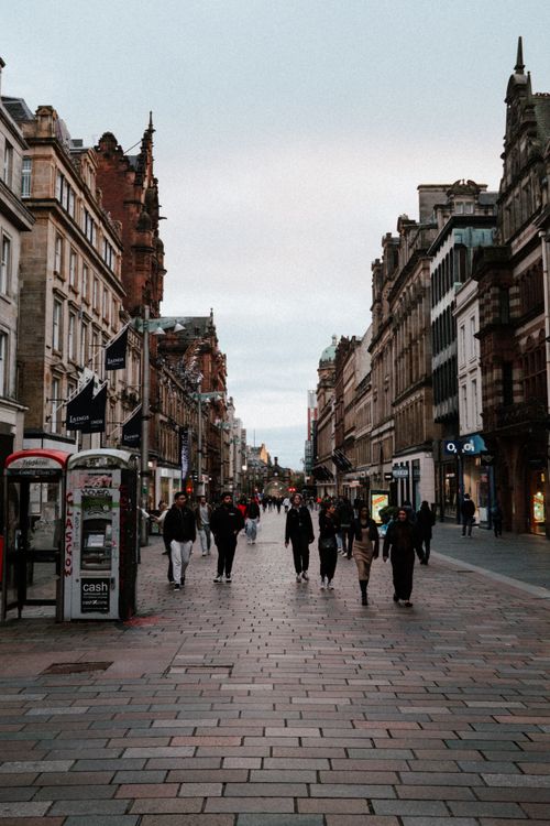 Free People walking down a lively street in Glasgow, Scotland, surrounded by historic architecture at dusk. Stock Photo