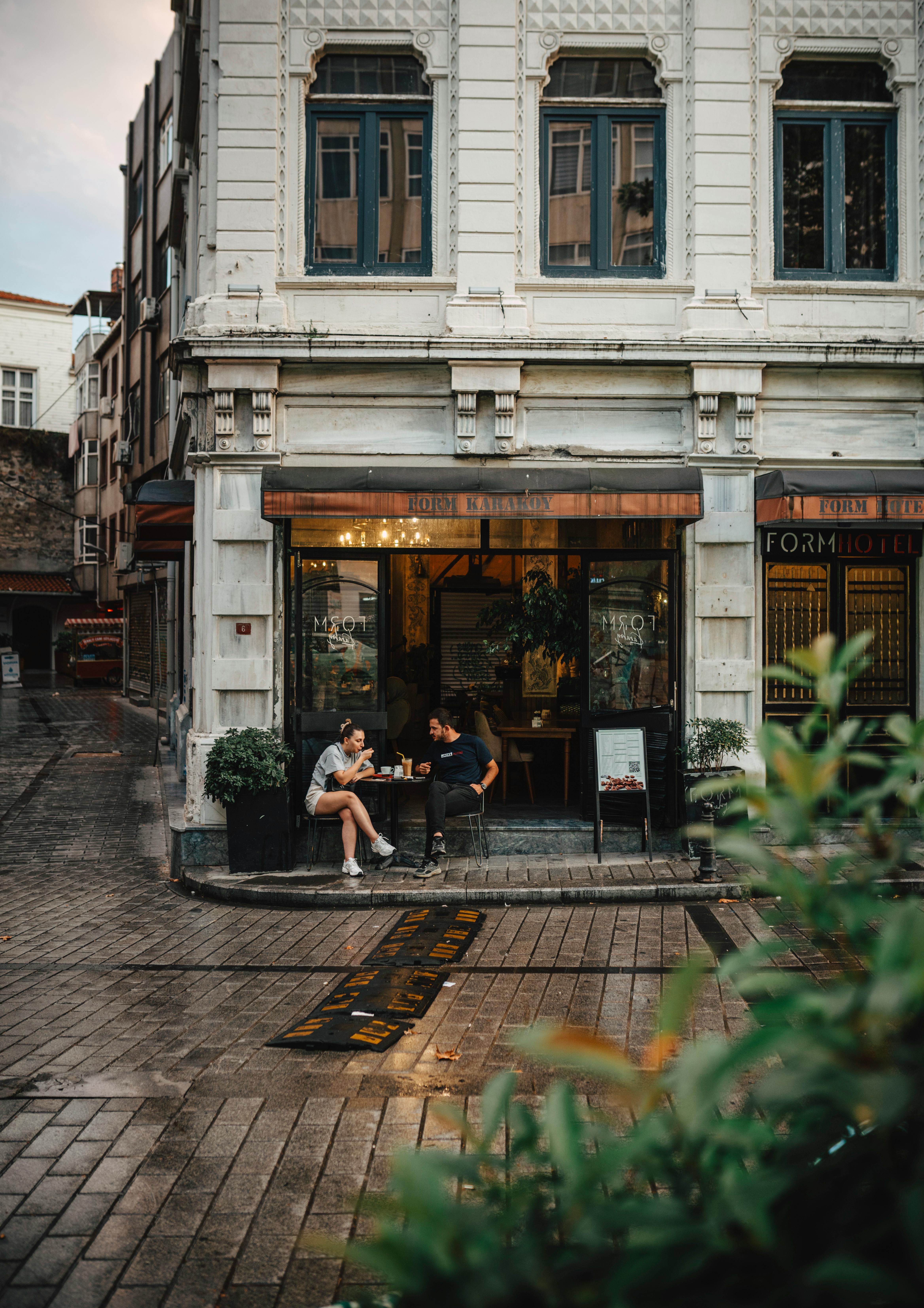Two people enjoy coffee at a quaint street cafe in a historic building setting.