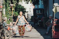 一位东亚老年妇女带着可回收物品走过北京街头，展现了城市生活的日常