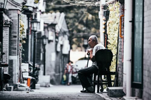 Free A senior man sits quietly in a historic alley in Beijing, capturing cultural ambiance. Stock Photo