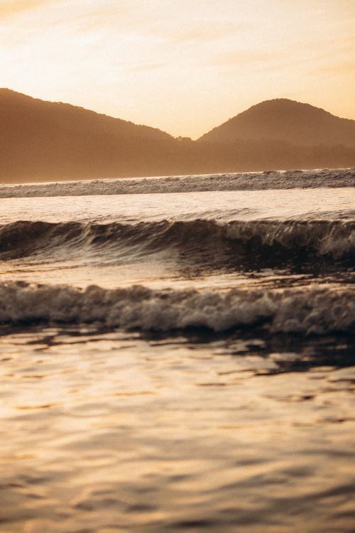 Free Peaceful ocean waves in the foreground with hills silhouetted by the warm sunset. Stock Photo