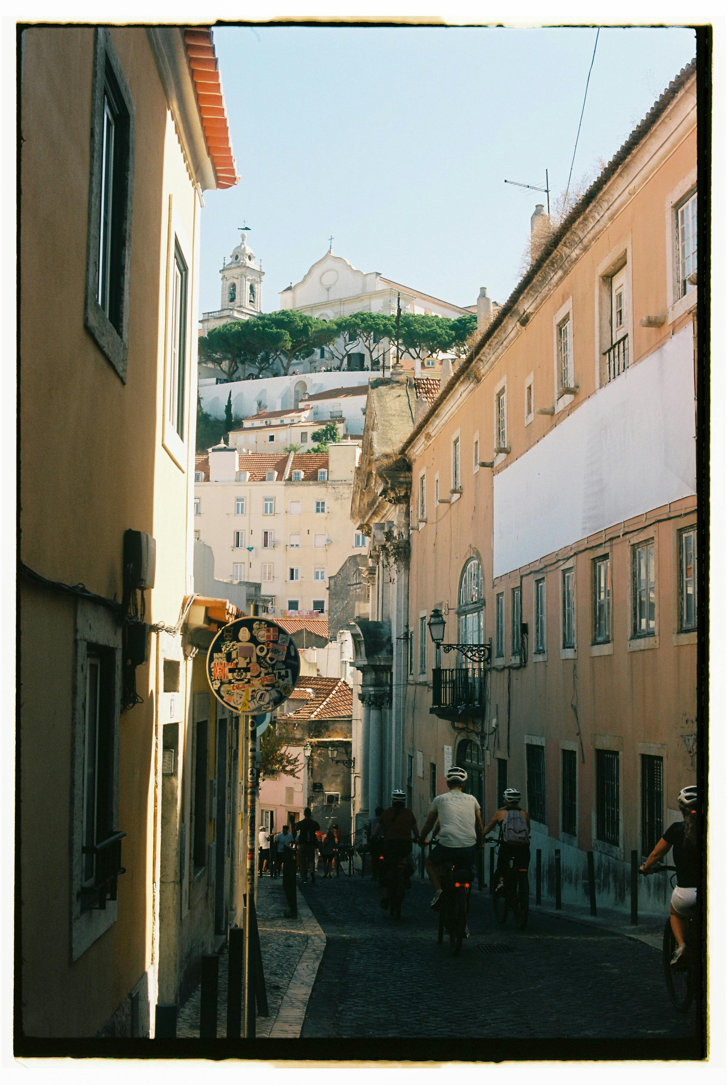 A picturesque street in Lisbon with cyclists and historic architecture under a clear blue sky.