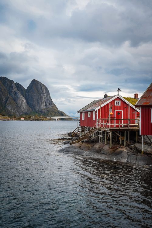 Free Picturesque red house on Lofoten coastline with dramatic mountain backdrop and calm sea. Stock Photo