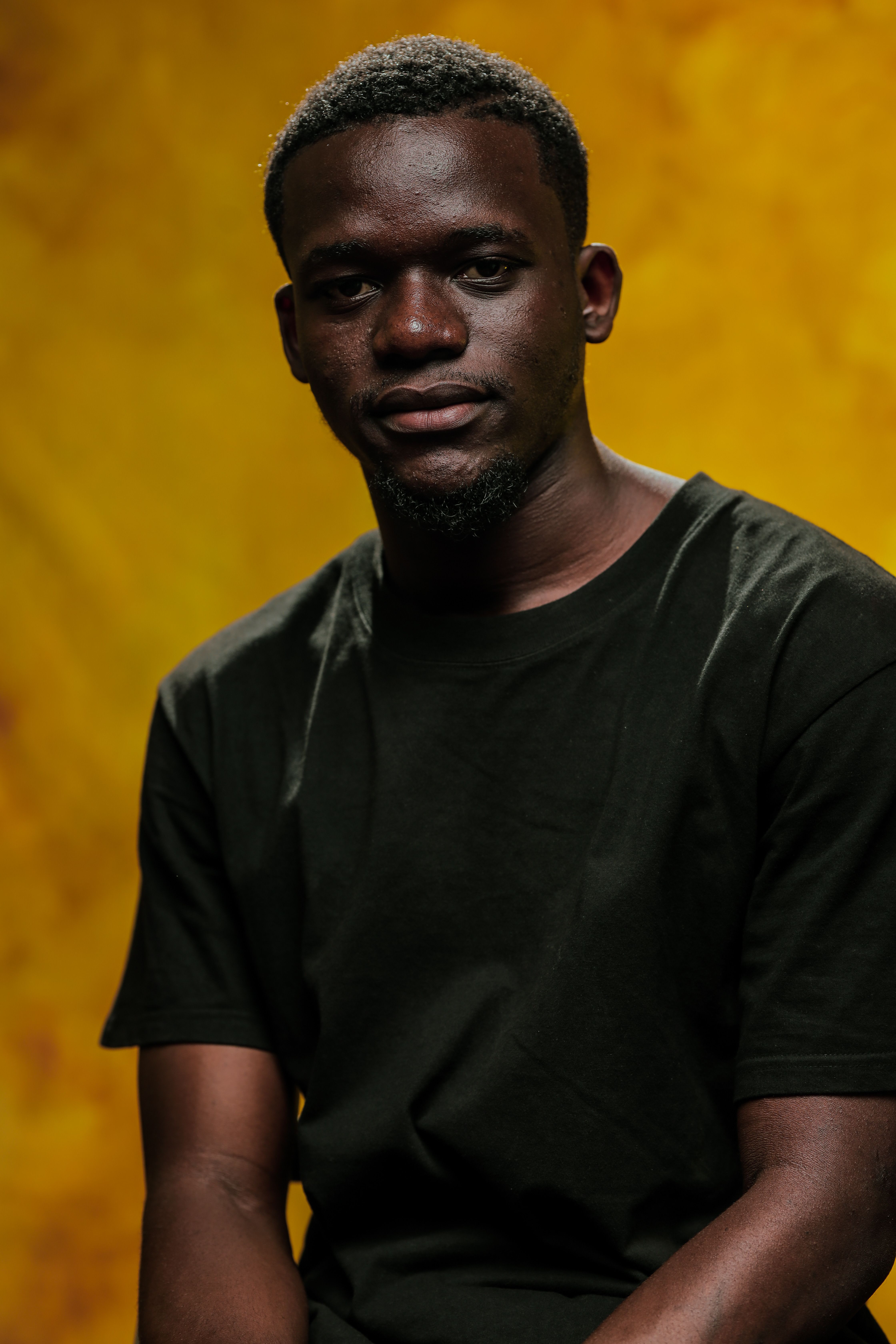 A thoughtful portrait of a man in a black shirt against a vibrant yellow backdrop.