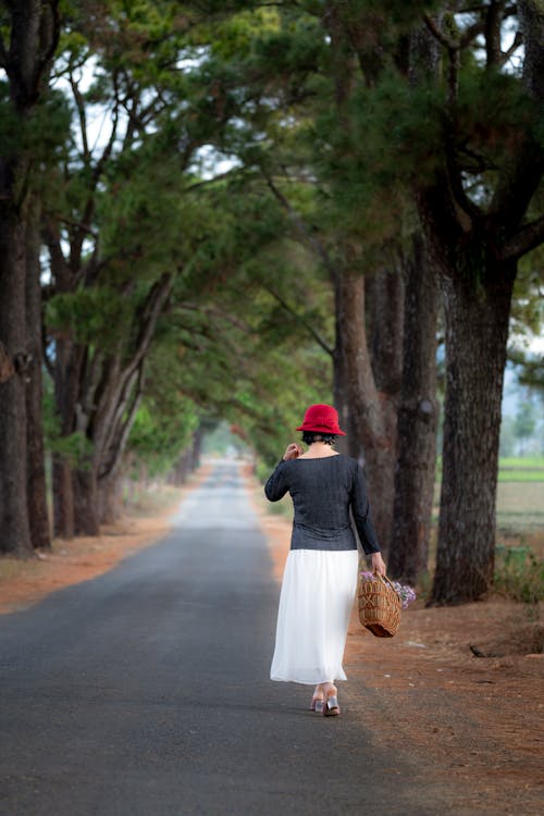 Woman Standing on Concrete Road at Middle of Trees