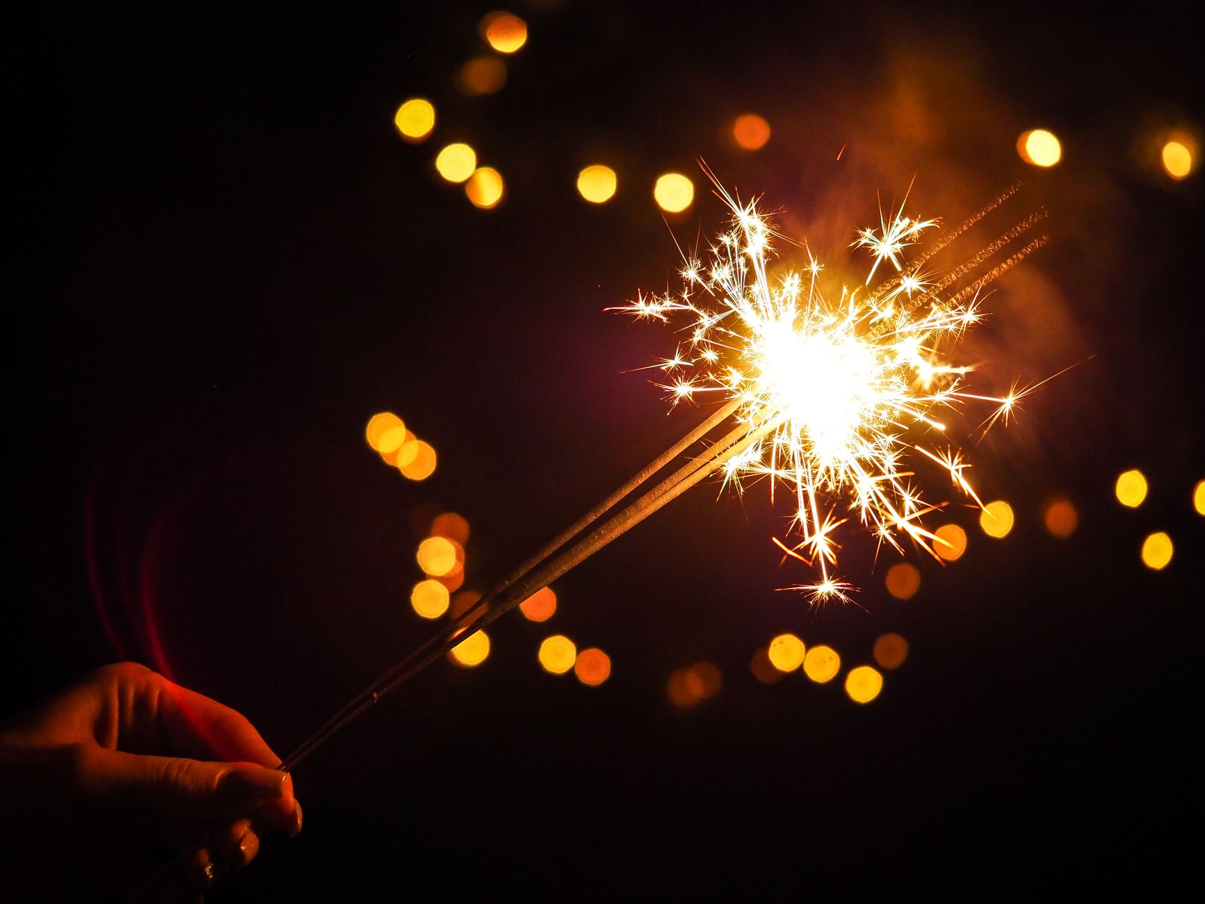 A vibrant sparkler glowing against a dark background with bokeh lights, symbolizing celebration.