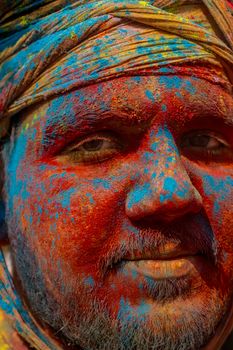 A vibrant portrait of a man covered in colorful powders during Holi in Mathura, India.