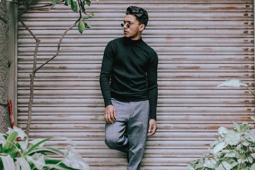 Free Fashionable young man in sunglasses posing confidently outdoors against metal shutter. Stock Photo