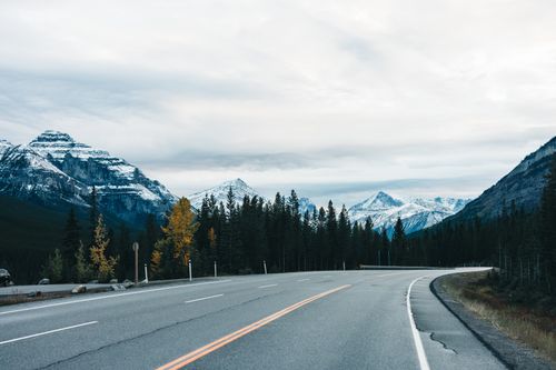 Free A winding road through the Canadian Rockies amidst colorful autumn trees and snow-capped peaks. Stock Photo