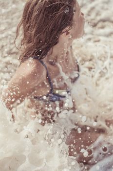 A young woman in a bikini enjoys the splashing ocean waves on a sunny summer day.