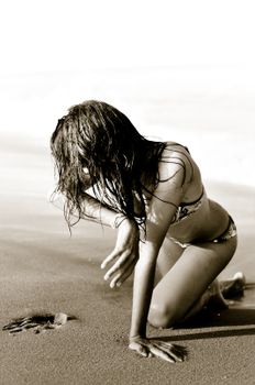 Woman on sandy beach in a swimsuit enjoying summer day, captured in sepia tone.