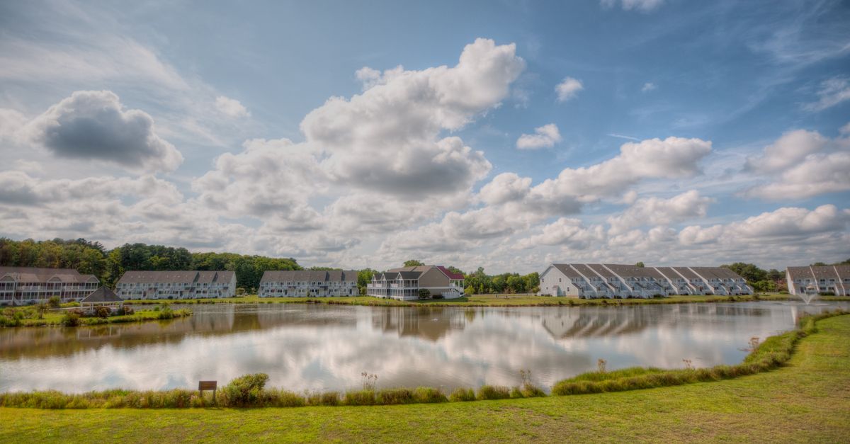 Expansive view of a suburban neighborhood by a calm lake under a cloudy sky.