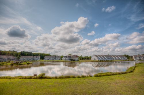 Free Expansive view of a suburban neighborhood by a calm lake under a cloudy sky. Stock Photo