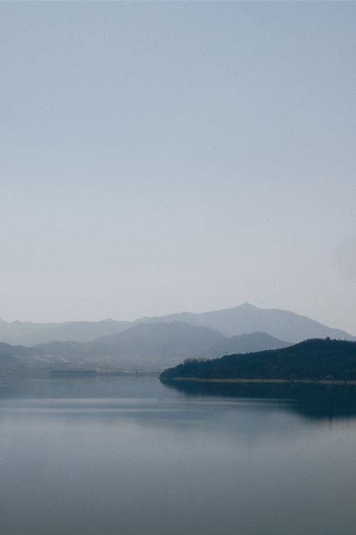 Free Tranquil lake with distant mountains under a clear sky, perfect for nature and travel imagery. Stock Photo