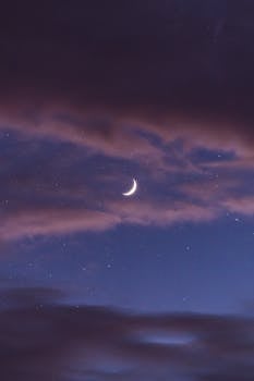Stunning view of a crescent moon surrounded by stars and clouds in the night sky.