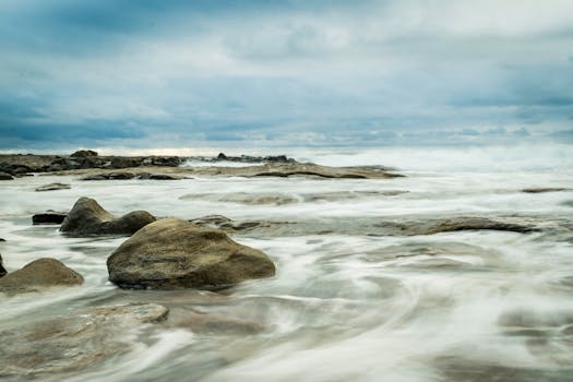 Serene coastal scene of rocks and gentle foamy waves under a cloudy dawn sky, capturing the tranquil beauty of nature.
