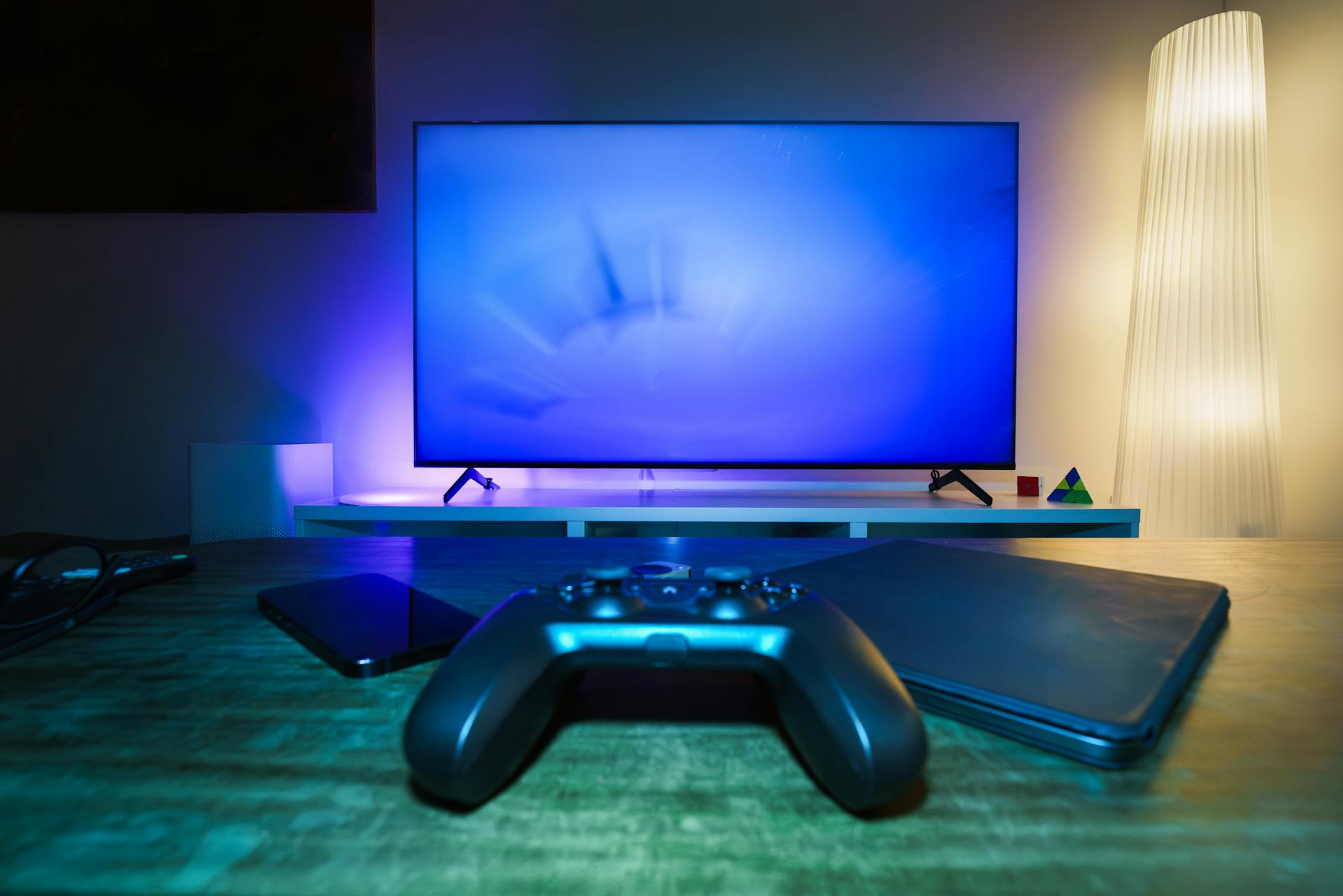 A stylish and ambient gaming setup featuring a controller, smart devices, and a TV in a lit living room.