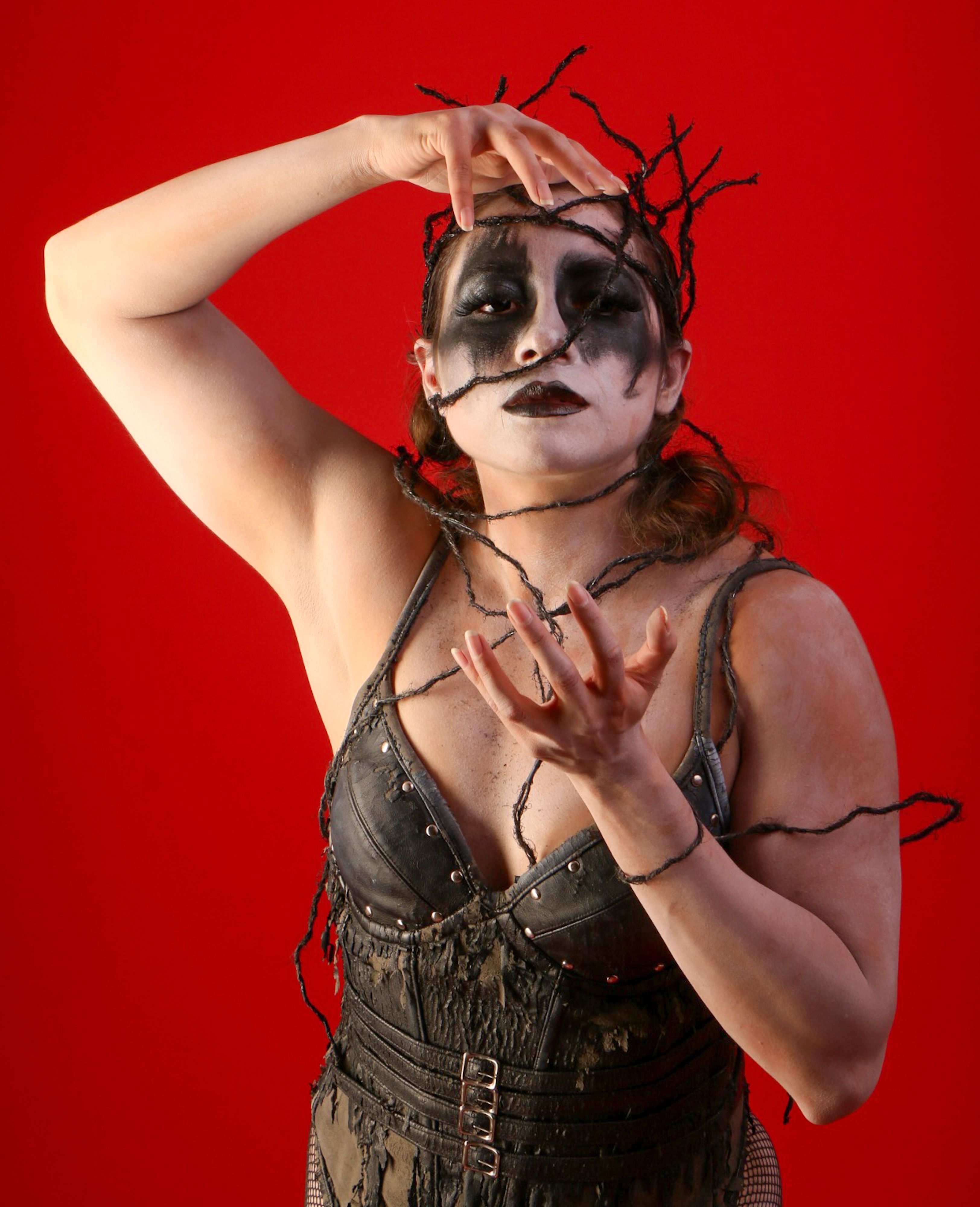 Gothic woman with creative makeup and costume on a red background posing dramatically.